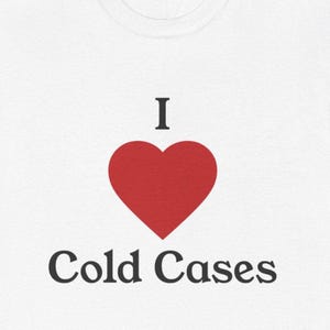 May include: A white t-shirt featuring a graphic design with the letter I in black, a solid red heart symbol in the center, and the words Cold Cases printed in black underneath the heart, all in a clean, bold, serif font style.