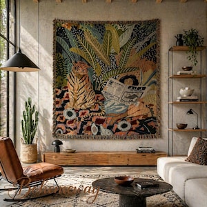 May include: A large tapestry featuring a tiger, lush foliage, and a person reading a newspaper. The tapestry has a fringed edge and is displayed on a neutral-colored wall. The room also includes a leather chair, a wooden cabinet, and a cactus.
