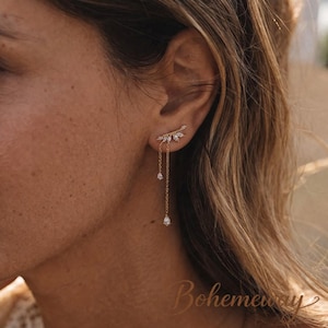 May include: Gold-coloured ear cuff featuring a leaf design and dangling teardrop-shaped crystals. The ear cuff is embellished with small, sparkling crystals, adding a touch of elegance. The jewellery is designed to be worn on the ear.