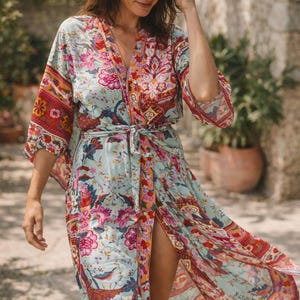 Può includere: Lunga vestaglia con motivo floreale nei toni del blu, rosa e arancione. La vestaglia ha maniche ampie e una cintura annodata. Il tessuto sembra leggero, adatto ai climi caldi. Il design include motivi floreali e di uccelli.