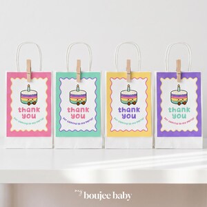 May include: Four white paper gift bags with handles, each featuring a scalloped-edge tag attached by a wooden clothespin. The tags display a colorful cartoon cake with a candle and the text "thank you for coming to my party!" in various colors.