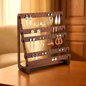 May include: A dark brown wooden earring display stand with multiple rows of slots, showcasing various earrings. The earrings include gold hoops, beaded dangles, and stud earrings. The stand is on a wooden table.