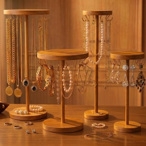 Op de afbeelding: Houten sieradenstandaards met diverse kettingen, armbanden en oorbellen. De standaards zijn rond met meerdere haken om sieraden op te hangen. De sieraden omvatten gouden kettingen, parelkettingen en edelsteen oorbellen. De standaards zijn van licht hout.