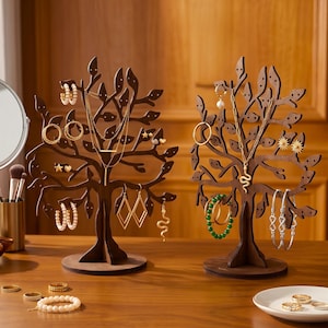 Peut inclure: Deux présentoirs à bijoux en bois en forme d'arbres, présentant divers colliers, boucles d'oreilles et bracelets. Les arbres sont bruns avec des découpes en forme de feuilles. Les bijoux comprennent des créoles dorées, des bracelets de perles et des bracelets de perles vertes.