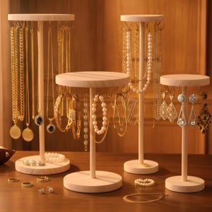 May include: Four wooden jewellery display stands of varying heights. The stands hold necklaces, bracelets, and earrings. The jewellery is gold and pearl. The stands are on a wooden surface. Rings and a bracelet are also on the surface.