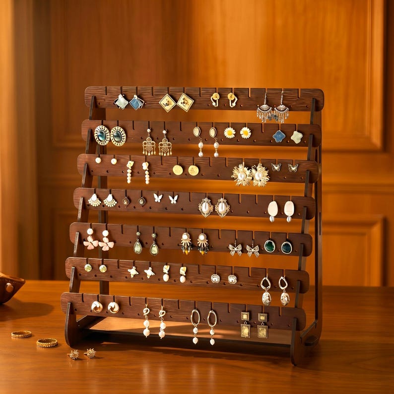 May include: A wooden earring display stand with multiple horizontal rows, showcasing various earrings. The stand is made of dark brown wood and is filled with a variety of earrings in different styles and colors. The earrings include studs, hoops, and dangling designs.