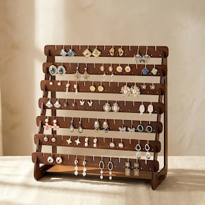May include: A dark brown wooden earring display stand filled with various earrings. The stand has multiple horizontal rows with small holes to hold the earrings. The earrings are of different styles, colors, and sizes, including studs, dangles, and hoops.