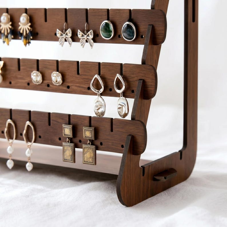 May include: A dark brown wooden earring display stand with multiple rows of slots for hanging earrings. Various earrings are displayed, including studs, hoops, and dangling styles. The stand has a modern, minimalist design, perfect for organizing and showcasing jewelry.