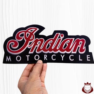 May include: Black and red embroidered patch with the text "Indian MOTORCYCLE" in a stylized font. The word "Indian" is in red with a white outline, and "MOTORCYCLE" is in white. The patch is held by a hand.