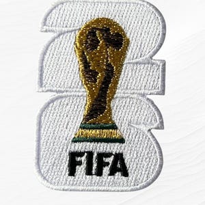 May include: Embroidered patch featuring the FIFA World Cup trophy in gold, set against a white background shaped like the number 23. The word "FIFA" is embroidered in black at the bottom. The text "Dayan IMPEX" is in the upper left corner.