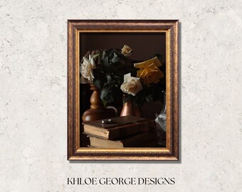 May include: A framed still life painting featuring a bouquet of yellow and white roses in a vase, with old books and a ring. The frame is a dark brown with gold accents. The text "KHOLE GEORGE DESIGNS" is at the bottom.
