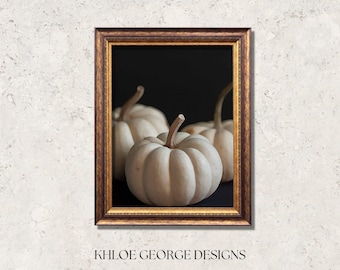 May include: Three white pumpkins arranged on a black background. The pumpkins are smooth and have a slightly textured surface. The pumpkins are in a gold frame.