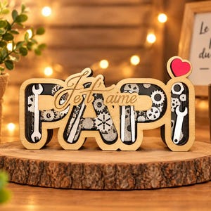 Peut inclure: Un objet décoratif en bois formant le mot PAPI en grandes lettres ajourées. L'intérieur des lettres contient des engrenages et des formes de clés mécaniques argentées. Le texte Je t'aime est superposé en écriture cursive avec un petit cœur rouge au-dessus du I.
