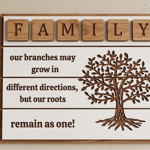 May include: A rectangular wooden wall sign featuring the word FAMILY in raised wooden tiles at the top. Below, white horizontal panels display the text: our branches may grow in different directions, but our roots remain as one! next to a tree.