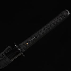 May include: Close-up of a black katana sword. The handle is wrapped in a textured black material with a diamond pattern. The blade guard and the blade itself are also black, creating a sleek, minimalist aesthetic.
