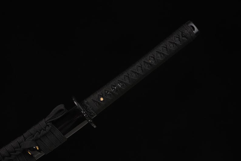 May include: Close-up of a black katana sword. The handle is wrapped in a textured black material with a diamond pattern. The blade guard and the blade itself are also black, creating a sleek, minimalist aesthetic.