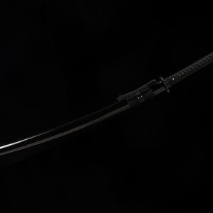 May include: A black katana sword with a curved blade. The handle is wrapped in a textured black material, and the scabbard is also black. The sword is set against a black background.