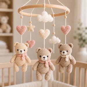 Puede incluir: Móvil para bebé hecho a mano con tres osos de peluche de ganchillo con bufandas rosas, suspendidos de un anillo de madera. El móvil también incluye corazones, estrellas y nubes de ganchillo en colores pastel.