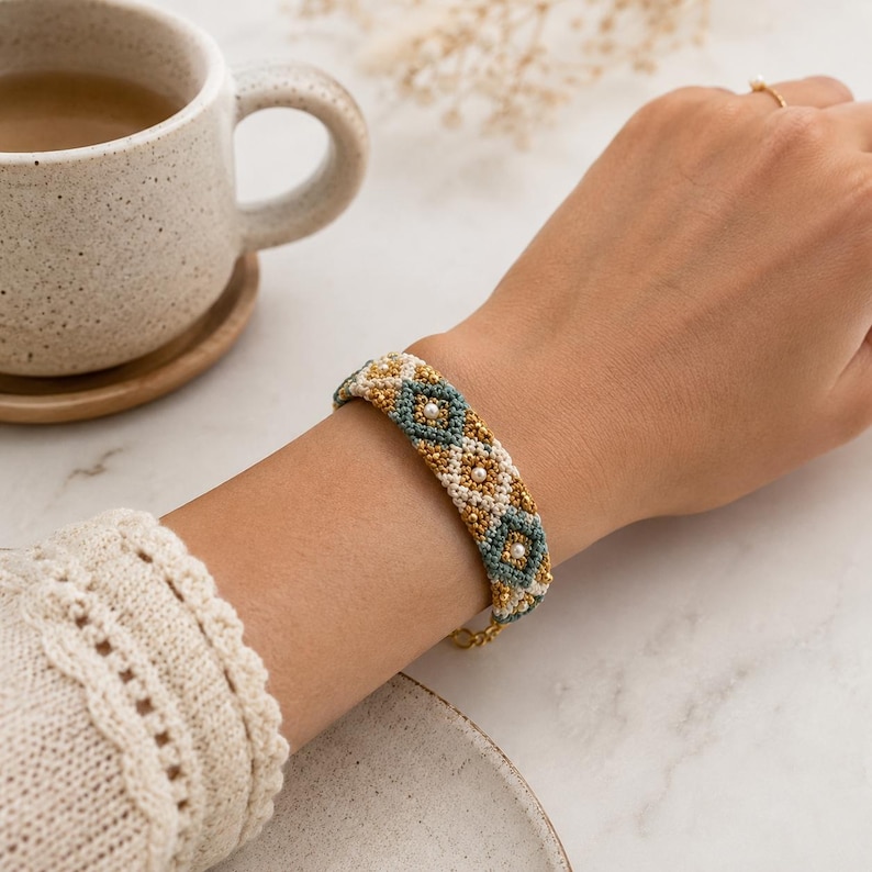 K&ouml;nnte beinhalten: Ein Armband mit Perlen in einem geometrischen Muster in Gold, T&uuml;rkis und Wei&szlig;. Das Armband wird am Handgelenk getragen und hat einen goldenen Kettenverschluss. Das Design umfasst kleine, perlenartige Perlen.