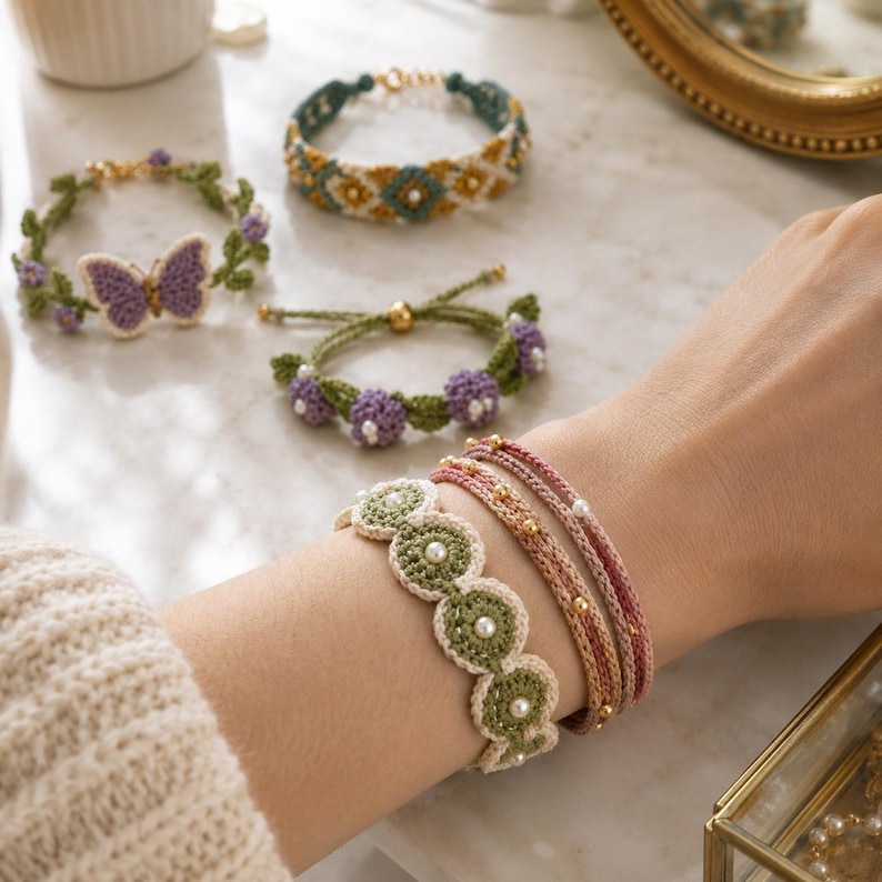 K&ouml;nnte beinhalten: Eine Sammlung handgefertigter H&auml;kelarmb&auml;nder in verschiedenen Designs. Die Armb&auml;nder weisen Blumen-, Schmetterlings- und Perlenakzente in Gr&uuml;n-, Lila- und Cremet&ouml;nen auf. Einige Armb&auml;nder sind mit Perlen und goldfarbenen Perlen verziert.