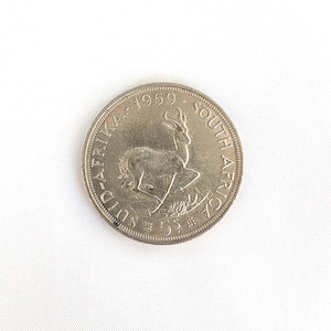 Puede incluir: Una moneda de plata de Sudáfrica, fechada en 1959. La moneda presenta un antílope springbok en el centro, con las palabras "SUID-AFRIKA" y "SOUTH AFRICA" alrededor del borde. También es visible la denominación "5S".