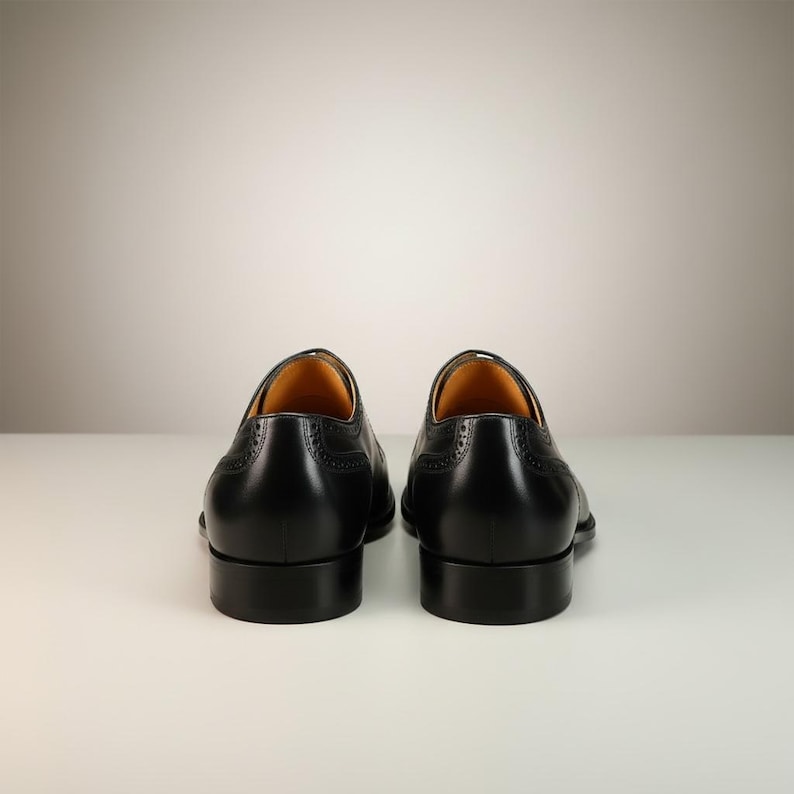 May include: A pair of black leather dress shoes with a classic design. The shoes have a low heel and decorative perforations along the edges. The interior is a light tan color.