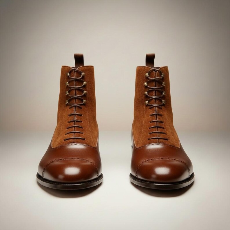 May include: A pair of brown leather and suede boots with a cap toe design. The boots have a lace-up closure with brown laces and a pull tab at the top. The boots are displayed on a white background.
