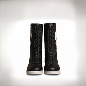 K&ouml;nnte beinhalten: Ein Paar schwarze wadenhohe Stiefel mit durchgehender Schn&uuml;rung vorne, schwarzen Schn&uuml;rsenkeln, einer strukturierten lederartigen Oberfl&auml;che und einer massiven wei&szlig;en Gummisohle. Ein gro&szlig;es wei&szlig;es kreisf&ouml;rmiges Logo ist an der Au&szlig;enseite.