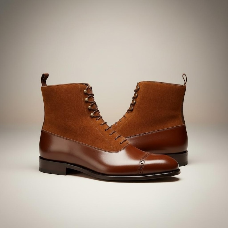 May include: A pair of brown leather boots with a cap toe design. The boots have a suede upper and a polished leather lower section. They feature a lace-up closure with metal eyelets and a pull tab at the back.