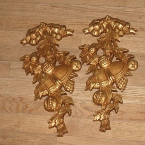 May include: A pair of gold-colored metal wall decor pieces featuring a stylized design of bells, leaves, and berries.