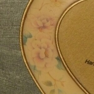 Puede incluir: Un marco de fotos en forma de coraz&oacute;n con un borde dorado y un dise&ntilde;o floral. El marco est&aacute; decorado con flores de color rosa pastel, amarillo y azul.