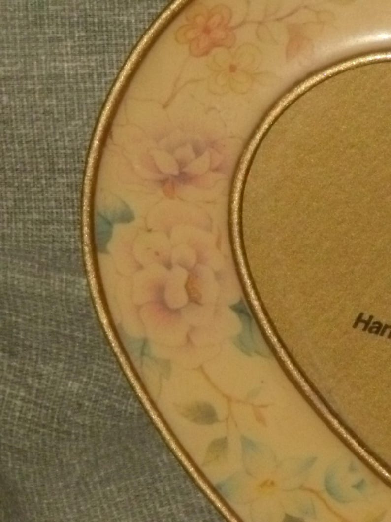 Puede incluir: Un marco de fotos en forma de coraz&oacute;n con un borde dorado y un dise&ntilde;o floral. El marco est&aacute; decorado con flores de color rosa pastel, amarillo y azul.