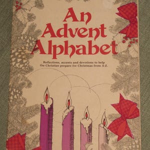 May include: A book titled An Advent Alphabet with a beige cover featuring red text, four lit candles in shades of purple and pink, red plaid bows, and gray pine branch illustrations. The subtitle reads: Reflections, accents and devotions to help the Christian prepare for Christmas from A-Z.