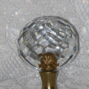 May include: A clear glass finial with a faceted design and a gold metal base. The finial is round and has a smooth, polished surface.