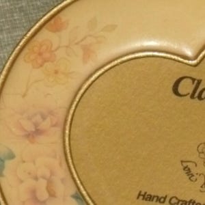 Puede incluir: Un marco de fotos en forma de coraz&oacute;n de color dorado con un dise&ntilde;o floral y el texto "Classic de Loni Michel & Hand Crafted" en la parte inferior.