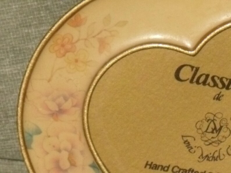 Puede incluir: Un marco de fotos en forma de coraz&oacute;n de color dorado con un dise&ntilde;o floral y el texto "Classic de Loni Michel & Hand Crafted" en la parte inferior.