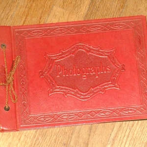 May include: A red leather photo album with a decorative border and the word "Photographs" embossed on the front.