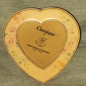 Puede incluir: Un marco de fotos en forma de coraz&oacute;n con un borde dorado y un dise&ntilde;o floral. El marco mide 3 1/2 pulgadas por 3 1/2 pulgadas y dice "Classique de L'Ancienne" y "Hand Crafted & Enameled".