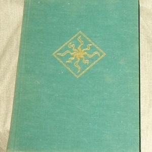 May include: A teal-colored book with a gold sunburst design inside a diamond shape on the cover. The book has a textured appearance and a white spine. The cover is slightly worn.