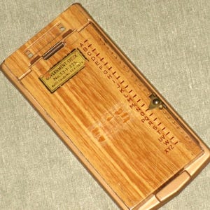 May include: A vintage wooden address book with a hinged lid and a metal clasp. The book features a series of alphabetical dividers and a label that reads "GOVERNMENT STOCK". The wood has a light brown grain.