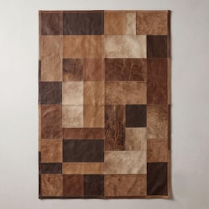 Puede incluir: Una alfombra rectangular compuesta por parches de cuero cosidos en varios tonos de marrón, que van desde el bronceado claro y crema hasta el chocolate oscuro. La superficie presenta una disposición en cuadrícula de paneles rectangulares y cuadrados.