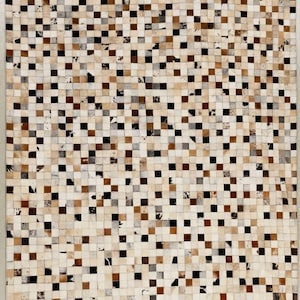 May include: A rectangular area rug constructed from a grid of small, square patches of animal hide. The patches feature a varied color palette of white, cream, tan, brown, dark brown, and black, with some pieces displaying natural mottled patterns.