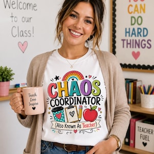 May include: A white t-shirt featuring a colorful graphic with a rainbow, a coffee cup, a clipboard, a pencil, and an apple. The text reads "CHAOS COORDINATOR" and "(Also Known As Teacher)". A light pink mug with "Teach Love Inspire" is held.