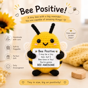 May include: A yellow and black crocheted bee plush toy holding a white rectangular sign that reads: Bee Positive, I may be a tiny bee, but I Bee-lieve in You! You're gonna BEE AWESOME. The bee has black antennae, small white wings, and black eyes.
