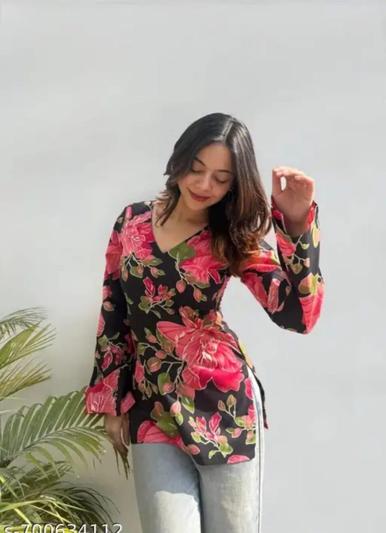 May include: A black floral print top with a V-neck and long sleeves. The top features a vibrant pink and green floral pattern. The garment is worn with light-colored pants.