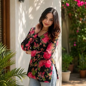 May include: Black long-sleeve top with a V-neck and a vibrant floral pattern in shades of pink and green. The top is paired with light blue denim jeans. The floral print is a prominent feature of the garment.