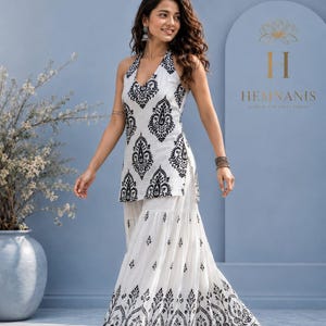 May include: A white sleeveless halter-neck tunic featuring a black paisley-inspired print paired with a matching white floor-length skirt that has a flared silhouette and a black decorative border pattern along the hemline.