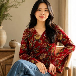 May include: A red floral print blouse with a V-neck and long sleeves. The blouse features a pattern of yellow and green flowers and leaves. The model is wearing blue jeans. The blouse has a small white tag with a black "S" on it.