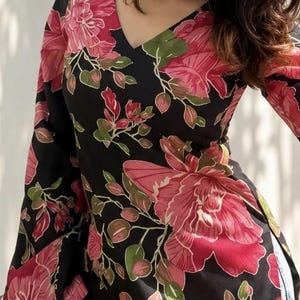 May include: Black top with a V-neck and long sleeves, adorned with a large floral pattern in shades of pink, red, and green. The flowers are set against a black background. The garment appears to be made of a lightweight fabric.