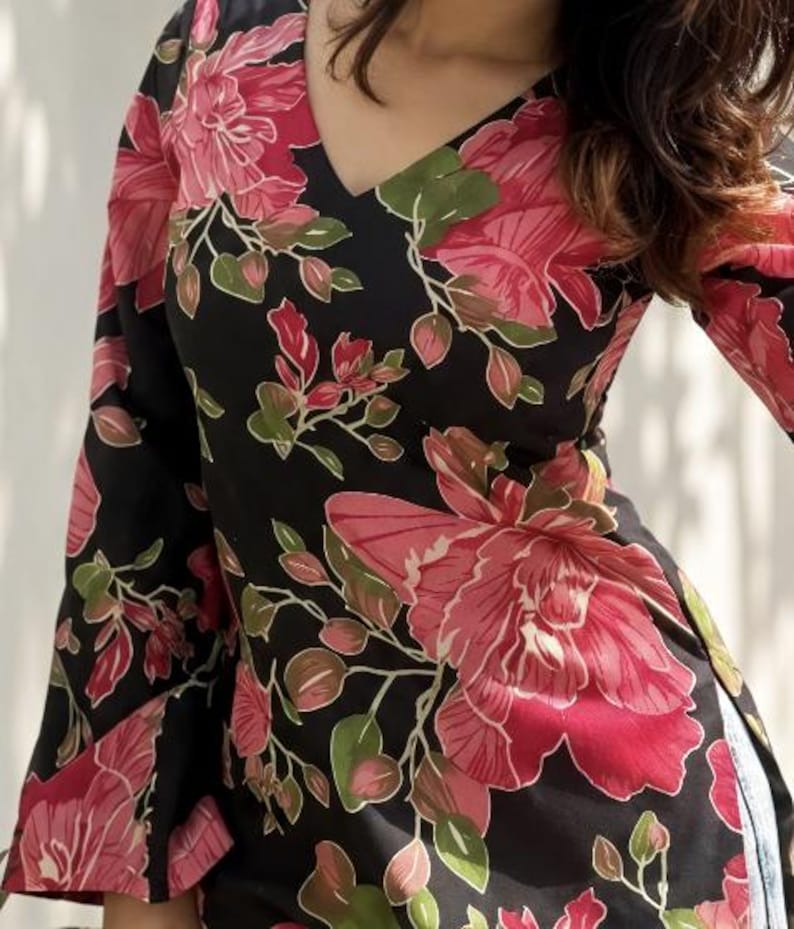 May include: Black top with a V-neck and long sleeves, adorned with a large floral pattern in shades of pink, red, and green. The flowers are set against a black background. The garment appears to be made of a lightweight fabric.